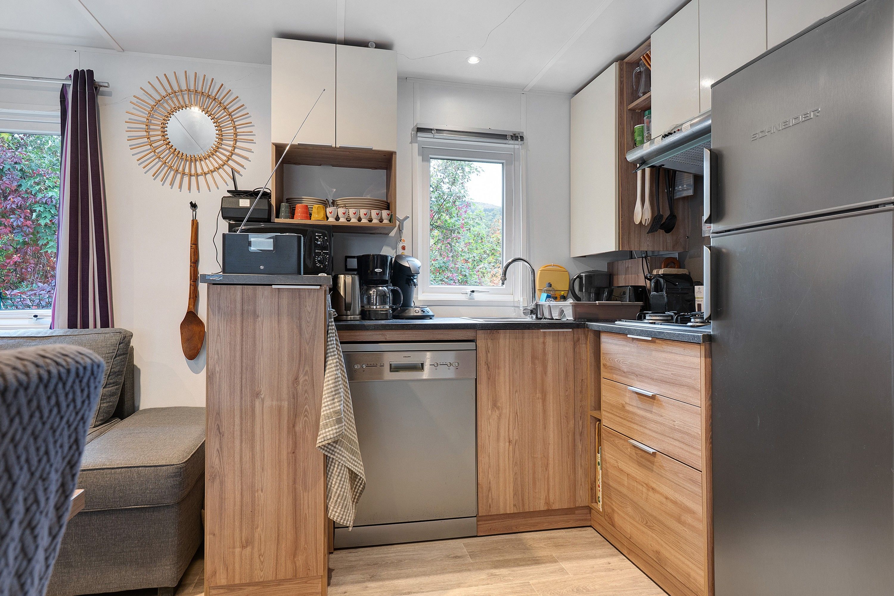 Cocina compacta con armarios de madera, lavavajillas empotrado y refrigerador de acero inoxidable.