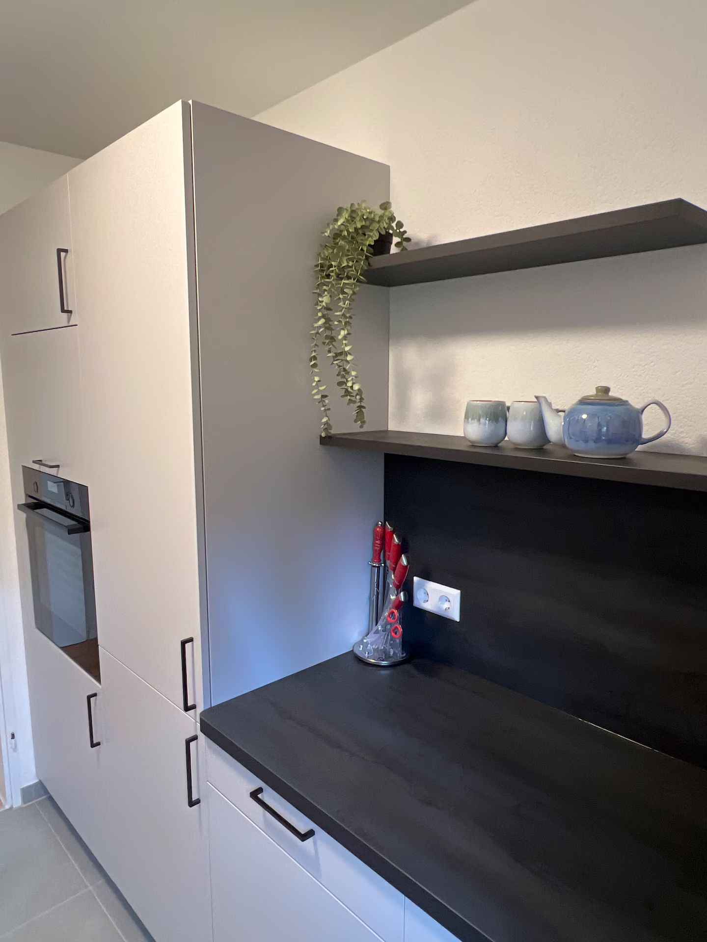Eine Küche mit Einbauofen, dunkler Arbeitsplatte und einem Regal mit Küchenutensilien.