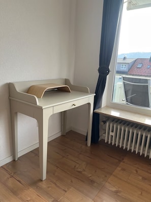 Ein Zimmer mit einem weißen Schreibtisch, einem Heizkörper und einem Fenster mit Blick auf Gebäude.