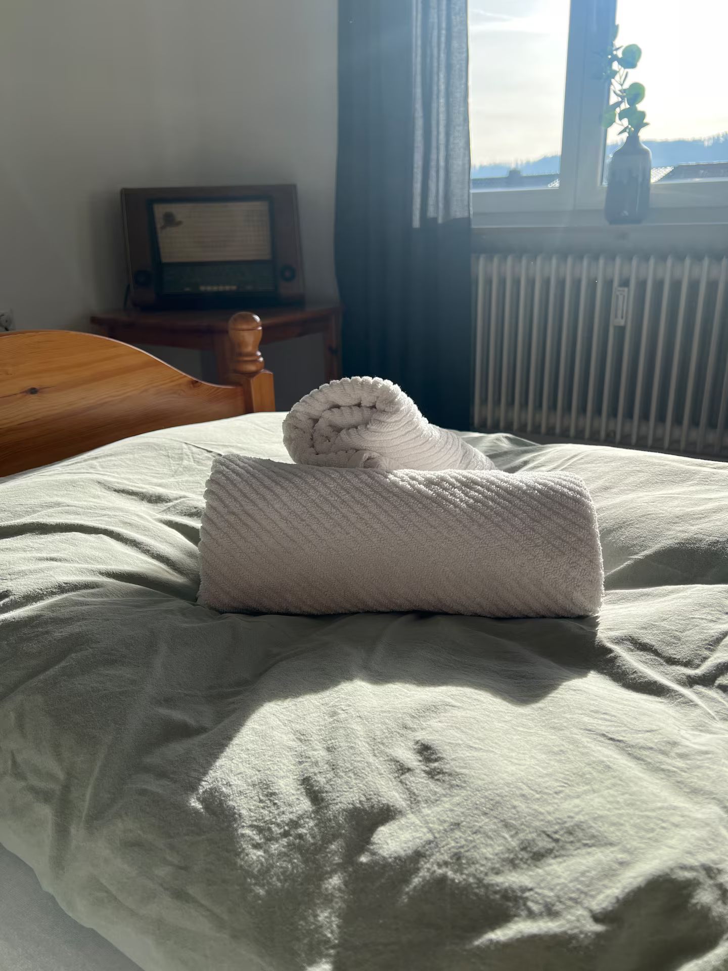 Ein Bett mit einem gefalteten weißen Handtuch und einem zusammengerollten Handtuch auf einer weißen Bettdecke.