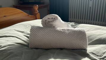Ein Bett mit einem gefalteten weißen Handtuch und einem zusammengerollten Handtuch auf einer weißen Bettdecke.