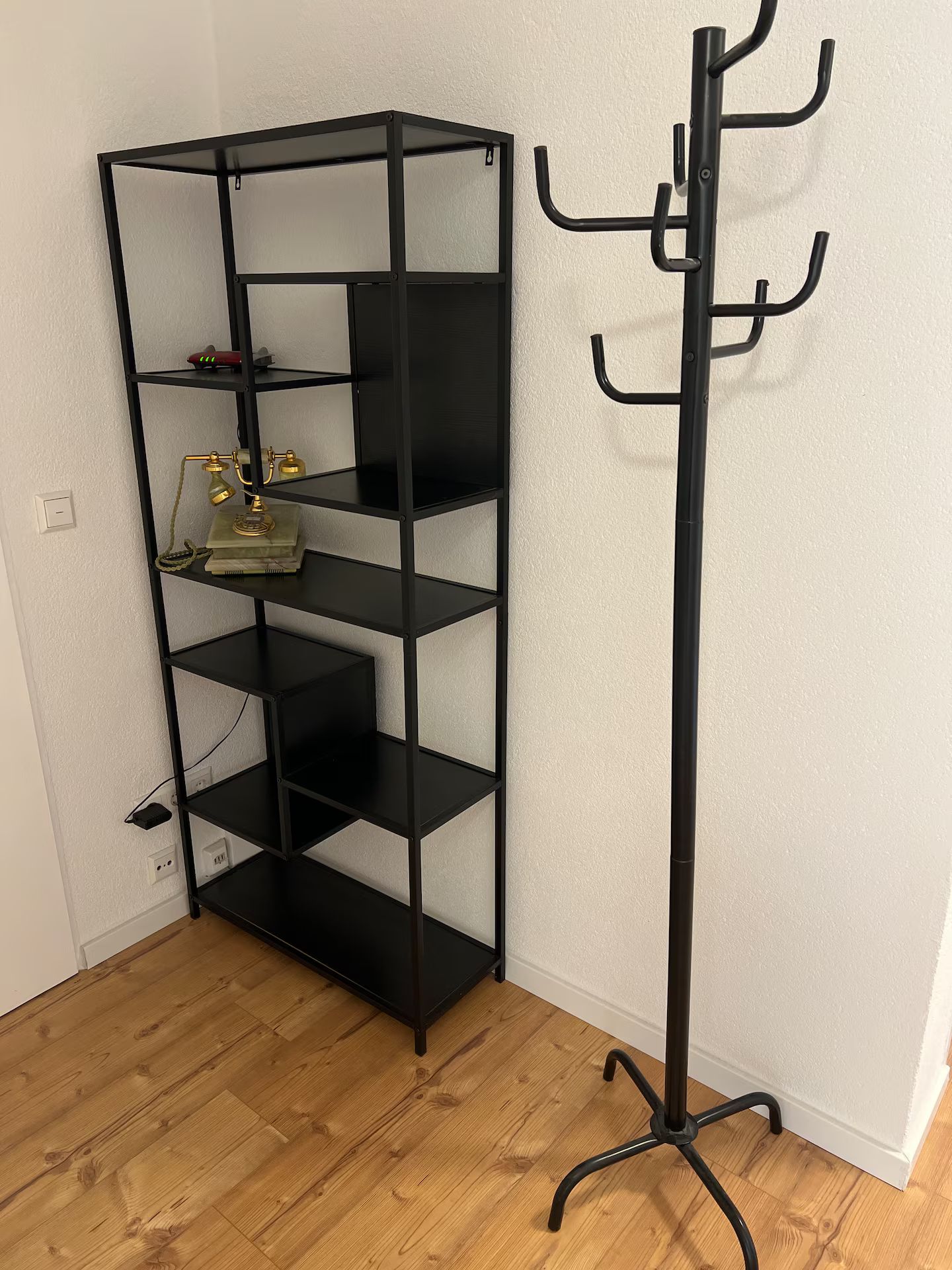 Eine schwarze Metallregaleinheit mit mehreren Fächern, ein schwarzer Kleiderständer mit Haken und ein Holzboden.