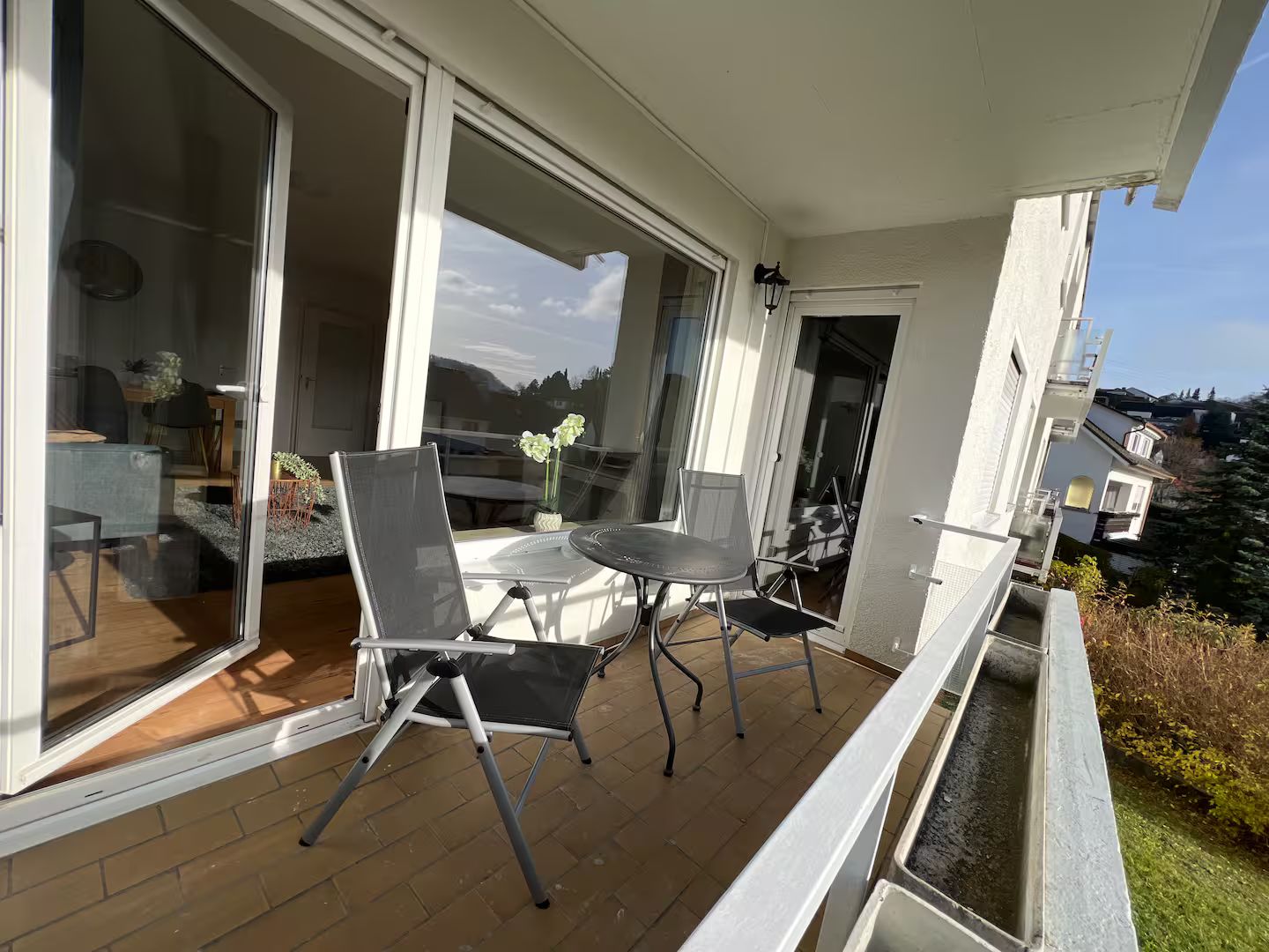 Ein Balkon mit Tisch und Stühlen, eine Schiebeglastür und Blick auf die Umgebung.