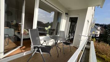 Ein Balkon mit Tisch und Stühlen, eine Schiebeglastür und Blick auf die Umgebung.