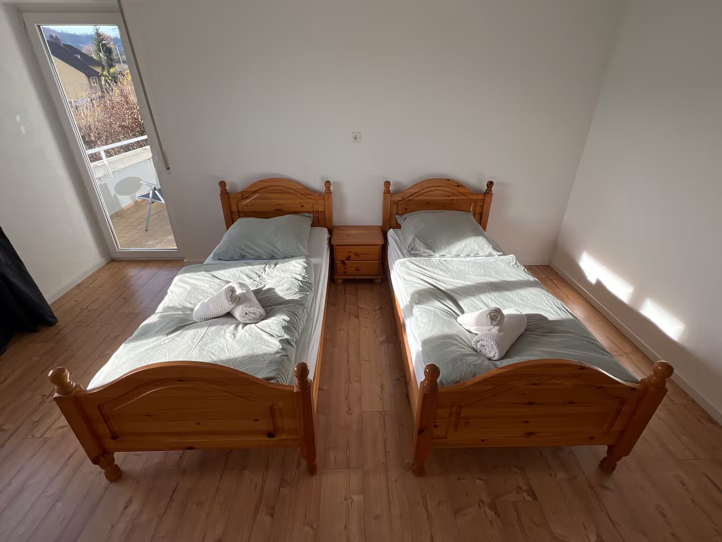 Ein Zimmer mit zwei hölzernen Betten, einem kleinen Nachttisch und einem großen Fenster.