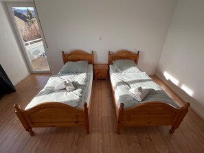 Ein Zimmer mit zwei hölzernen Betten, einem kleinen Nachttisch und einem großen Fenster.
