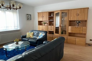 Ein Wohnzimmer mit einem Ledersofa, einem Glastisch und einer Holzkassette mit Glastüren.