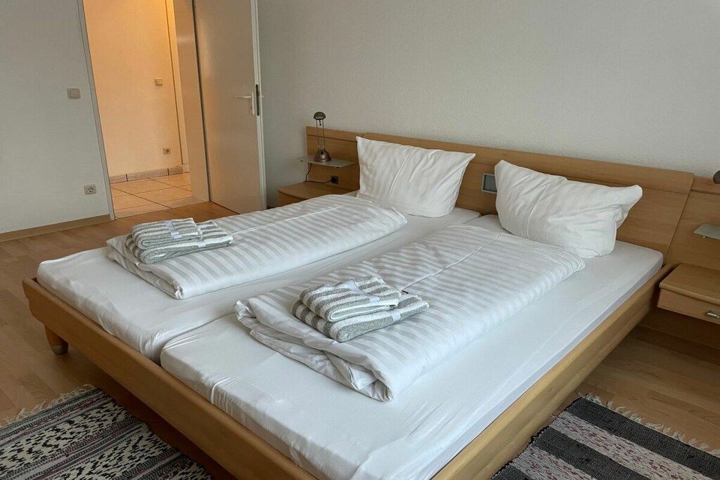 A double bed with white linens and striped towels, wooden headboard, bedside tables, and a patterned rug.