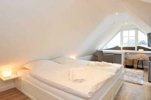 Ein Schlafzimmer mit Bett, Nachttisch, Lampe und Blick ins Freie.