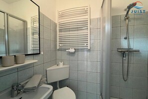 A bathroom with a toilet, sink, mirror, towel rack, and a shower with a handheld showerhead. - 331 - Holiday Apartment 1 (Juist)