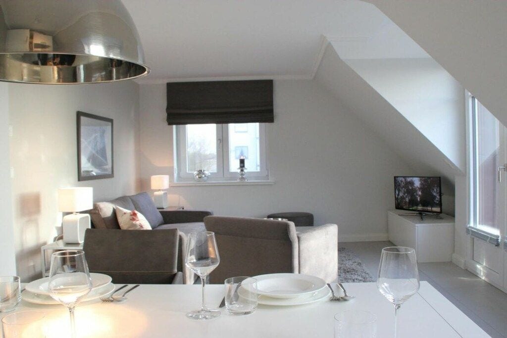 A modern living room with a dining area, a sofa set, a television, and a dining table set for two.