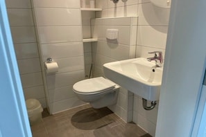 Ein kleines Badezimmer mit Toilette, Waschbecken und Toilettenpapierhalter an der Wand.