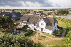 A traditional white house with a thatched roof, surrounded by greenery and a road. - Witthüs 15 - stylish living under a thatched roof (Wenningstedt)