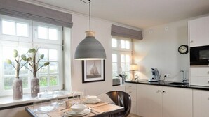 Une cuisine moderne avec des meubles blancs, une table à manger pour quatre personnes et un luminaire suspendu au-dessus.