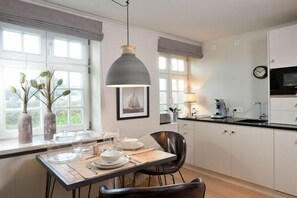 A modern kitchen with white cabinets, a dining table set for four, and a pendant light above. - Witthüs 15 - stylish living under a thatched roof (Wenningstedt)