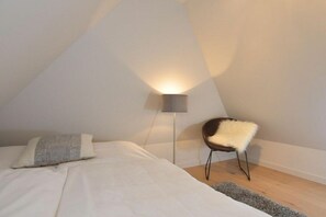 A bedroom with a bed, a chair, a floor lamp, and a rug. - Witthüs 15 - stylish living under a thatched roof (Wenningstedt)