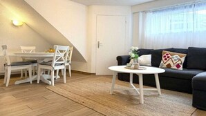 A living room with a sofa, a coffee table, and a dining area with chairs and a table. - Captain's House Apartment 2 (Cuxhaven-Duhnen)