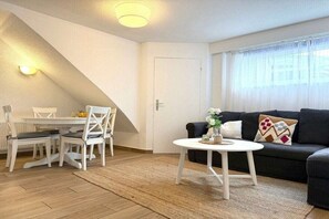 A living room with a sofa, a coffee table, and a dining area with chairs and a table. - Captain's House Apartment 2 (Cuxhaven-Duhnen)