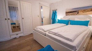 A bedroom with a bed, a wardrobe, and a painting on the wall. - Captain's House Apartment 2 (Cuxhaven-Duhnen)