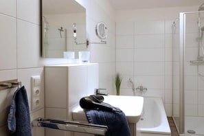 Un bagno moderno con un lavandino bianco, uno specchio, un portascopevoli e una zona doccia.