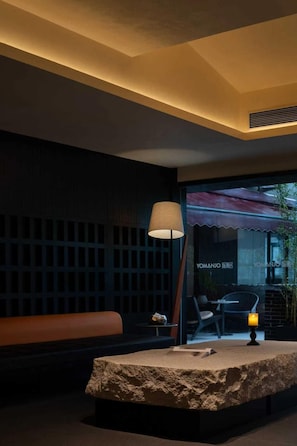 Un interior moderno con una recepción de textura de piedra, una lámpara y una zona de estar con un banco y una mesa.