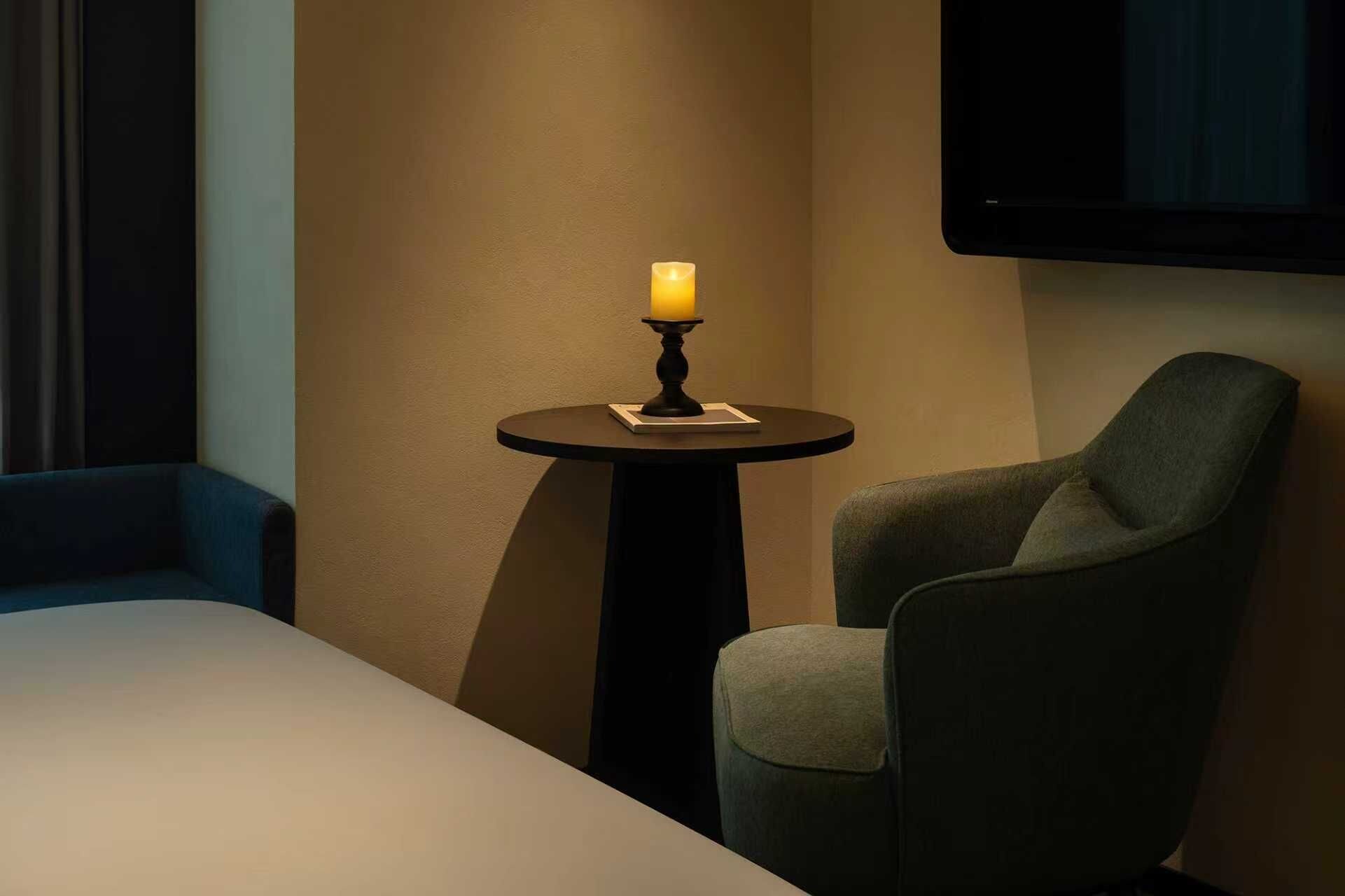 A hotel room with a bed, a small round table with a candle, and a single chair.