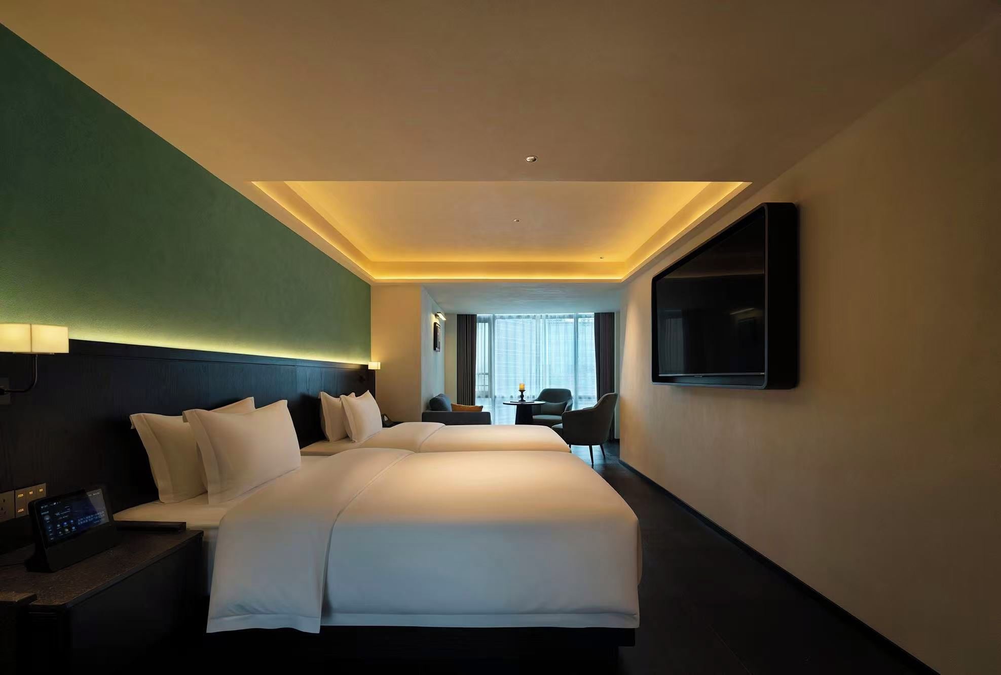 A hotel room with a large bed, bedside tables, a TV, and a view of the city through the window.