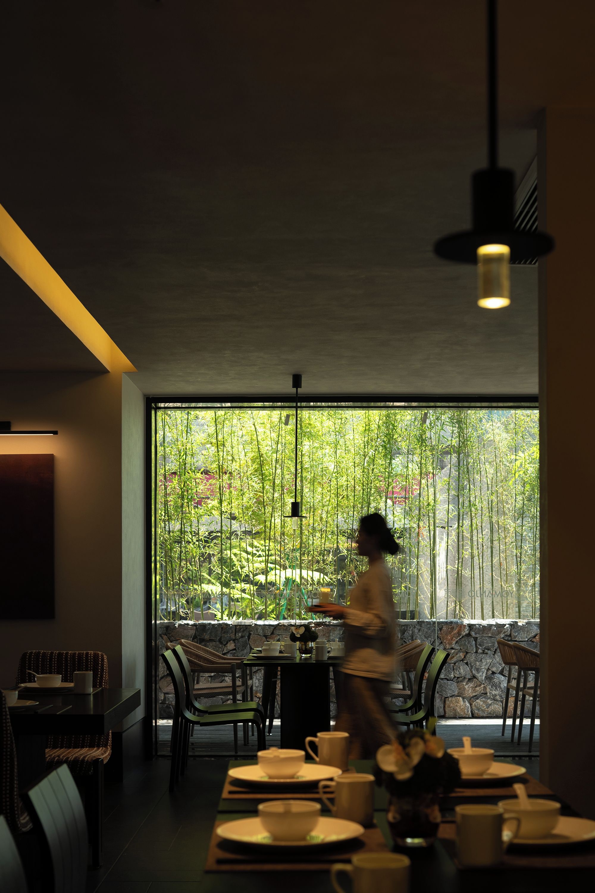 Un coin repas avec une table dressée pour deux personnes, des chaises et une grande fenêtre donnant sur un paysage verdoyant.