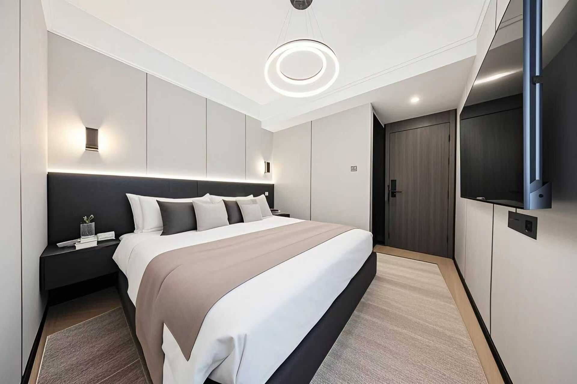 Une chambre d’hôtel moderne dotée d’un grand lit, d’un téléviseur à écran plat, d’une armoire et d’un luminaire au plafond.