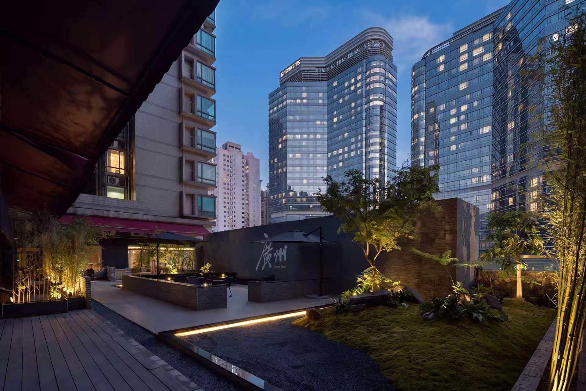 A modern urban courtyard with a seating area, a water feature, and tall buildings in the background.