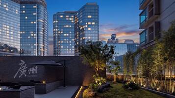 Eine moderne Stadtlandschaft mit Hochhäusern, einer begrünten Gartenanlage mit Steinen und Pflanzen sowie einer Sitzgelegenheit mit Bank und Tisch.