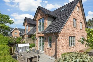 Ein Ziegelhaus mit geneigtem Dach, einer Terrasse mit Gartenmöbeln und einem Gartenbereich.