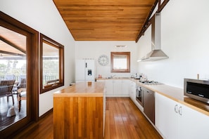 Una cocina moderna con piso de madera, gabinetes blancos, una campana extractora de acero inoxidable y un ventanal con vistas a una terraza.