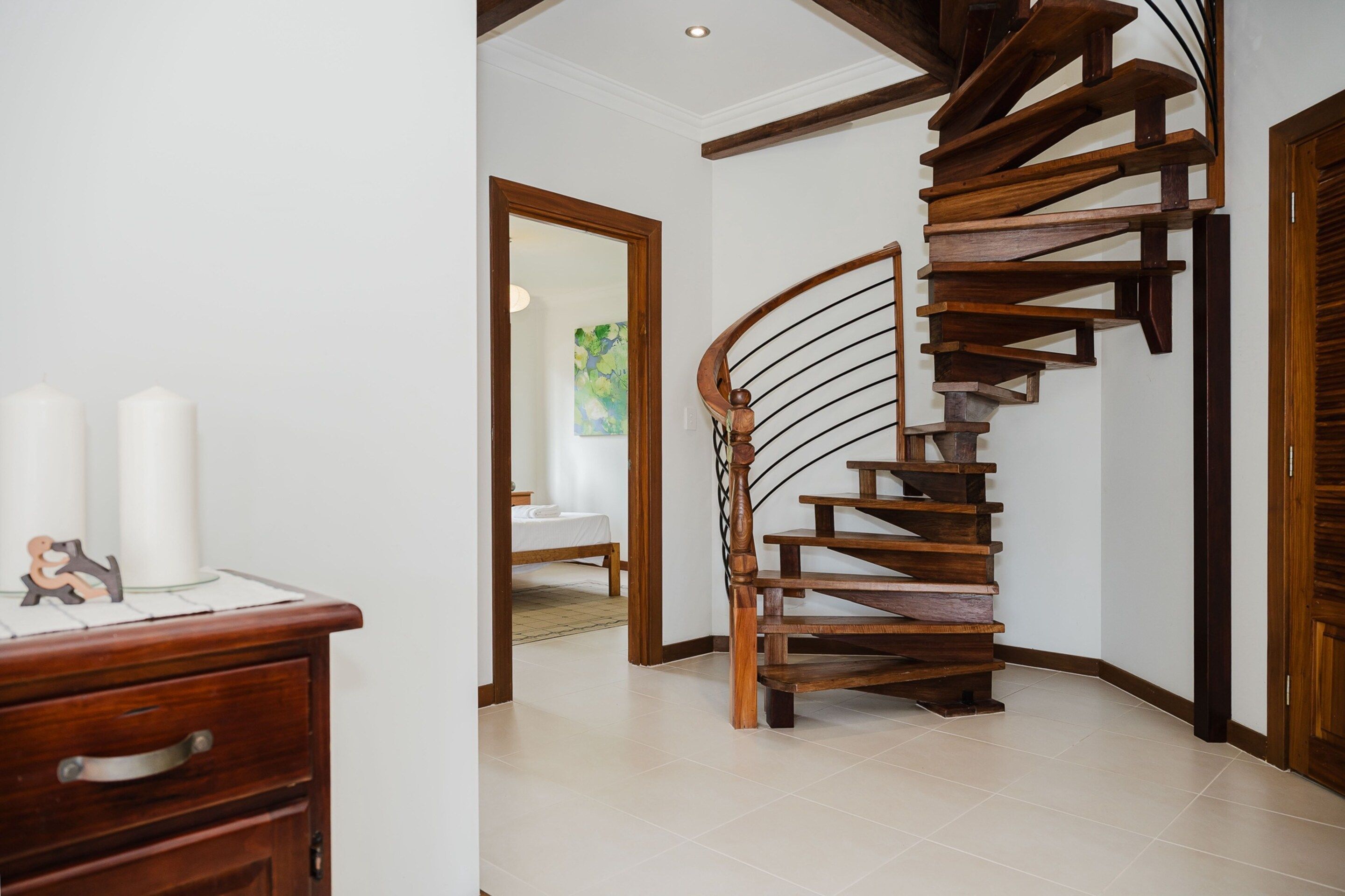 Una escalera de caracol con escalones de madera y barandilla, que conduce a un dormitorio con cama y un cuadro en la pared.