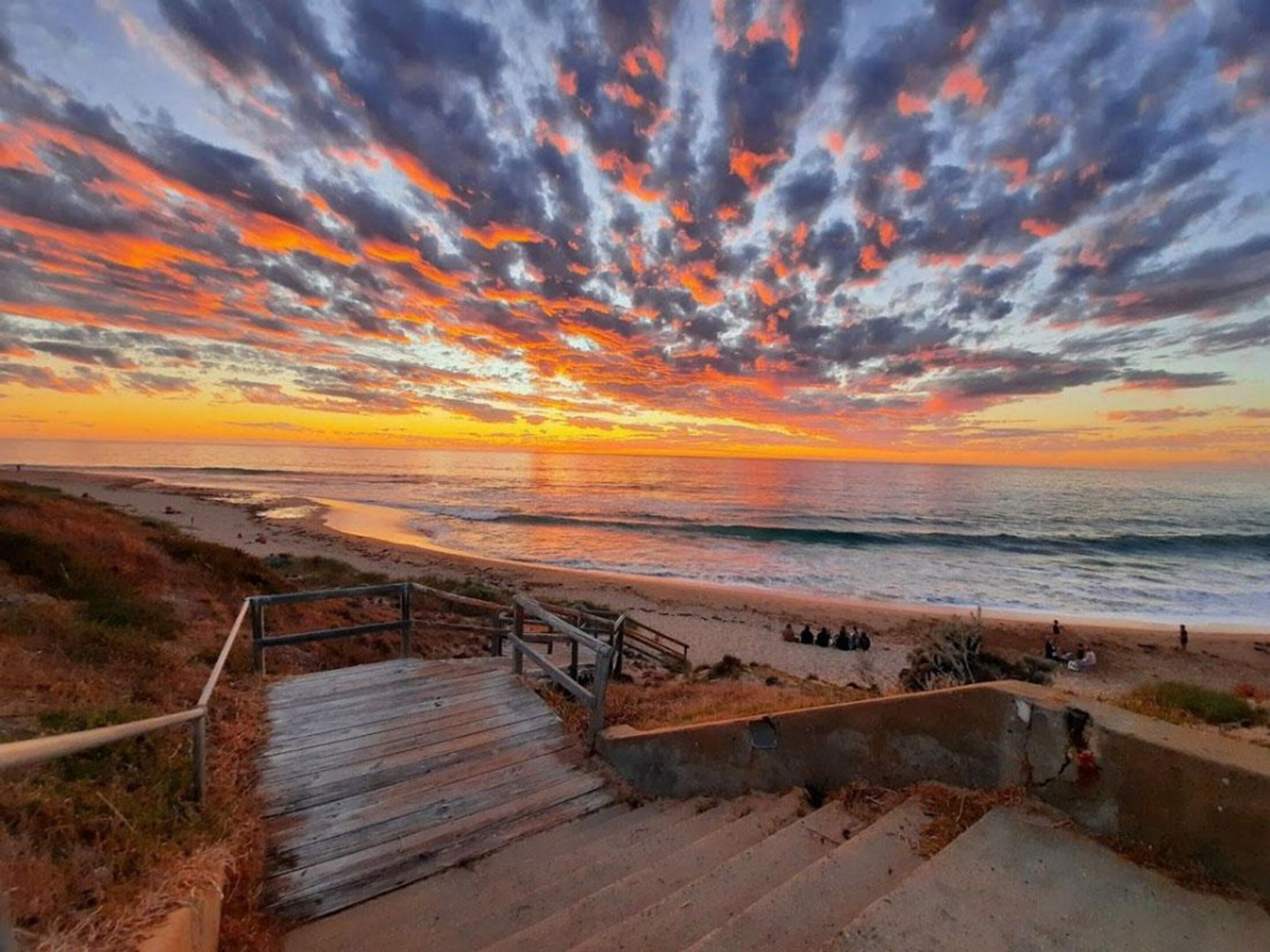 A wooden staircase leading down to a beach with a sunset in the background.