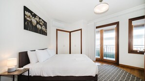 Ein Schlafzimmer mit Bett, Nachttisch, Lampe, Kunstwerk und Blick ins Freie.