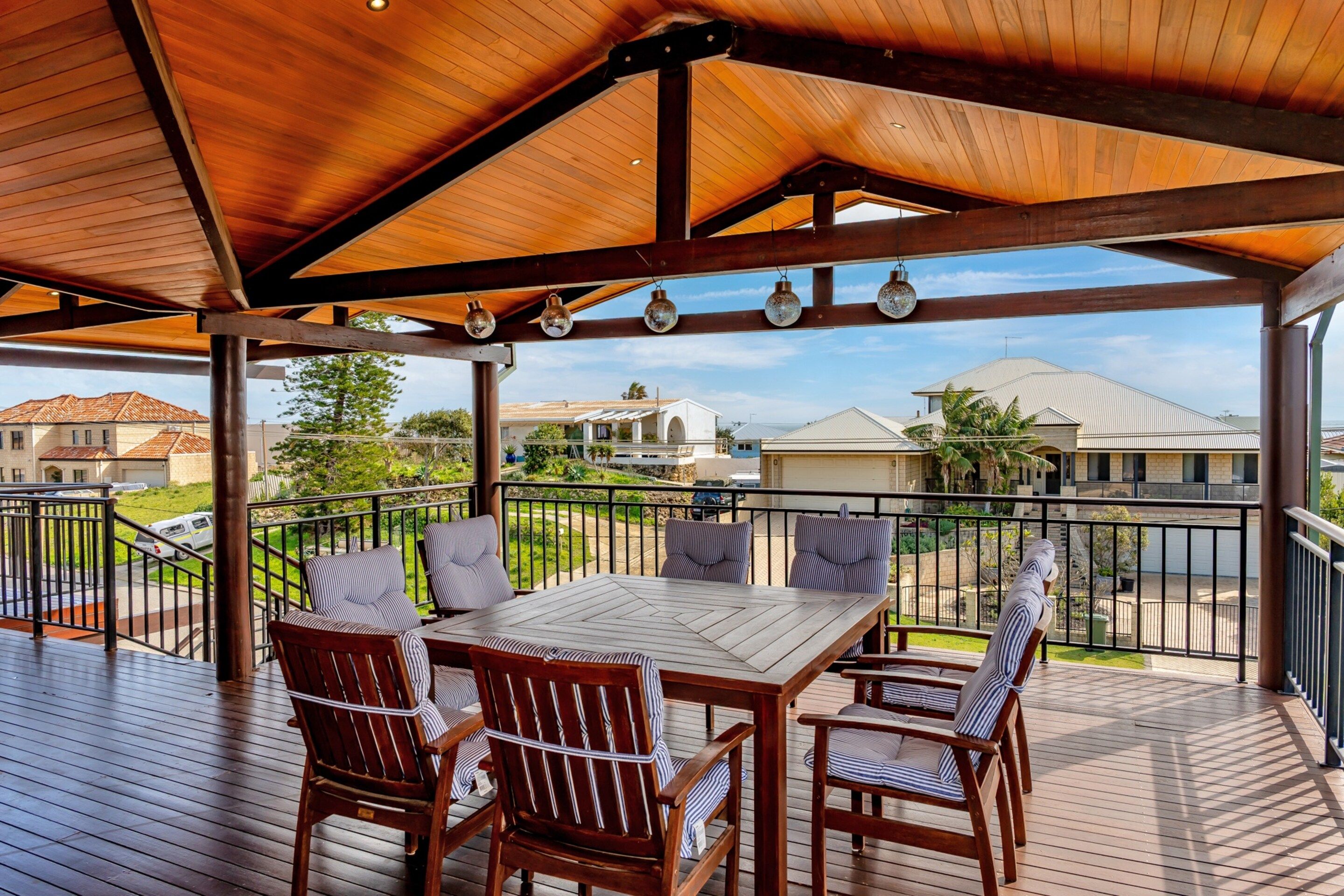 A covered outdoor deck with a wooden table and chairs, overlooking a residential area.