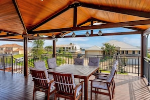 A covered outdoor deck with a wooden table and chairs, overlooking a residential area. - Ocean-view 3-bed House in Halls Head (Perth)