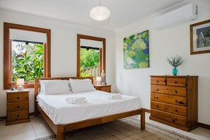 Un dormitorio con una cama de madera, dos mesitas de noche, un aparador y un ventanal grande, además de un cuadro en la pared.