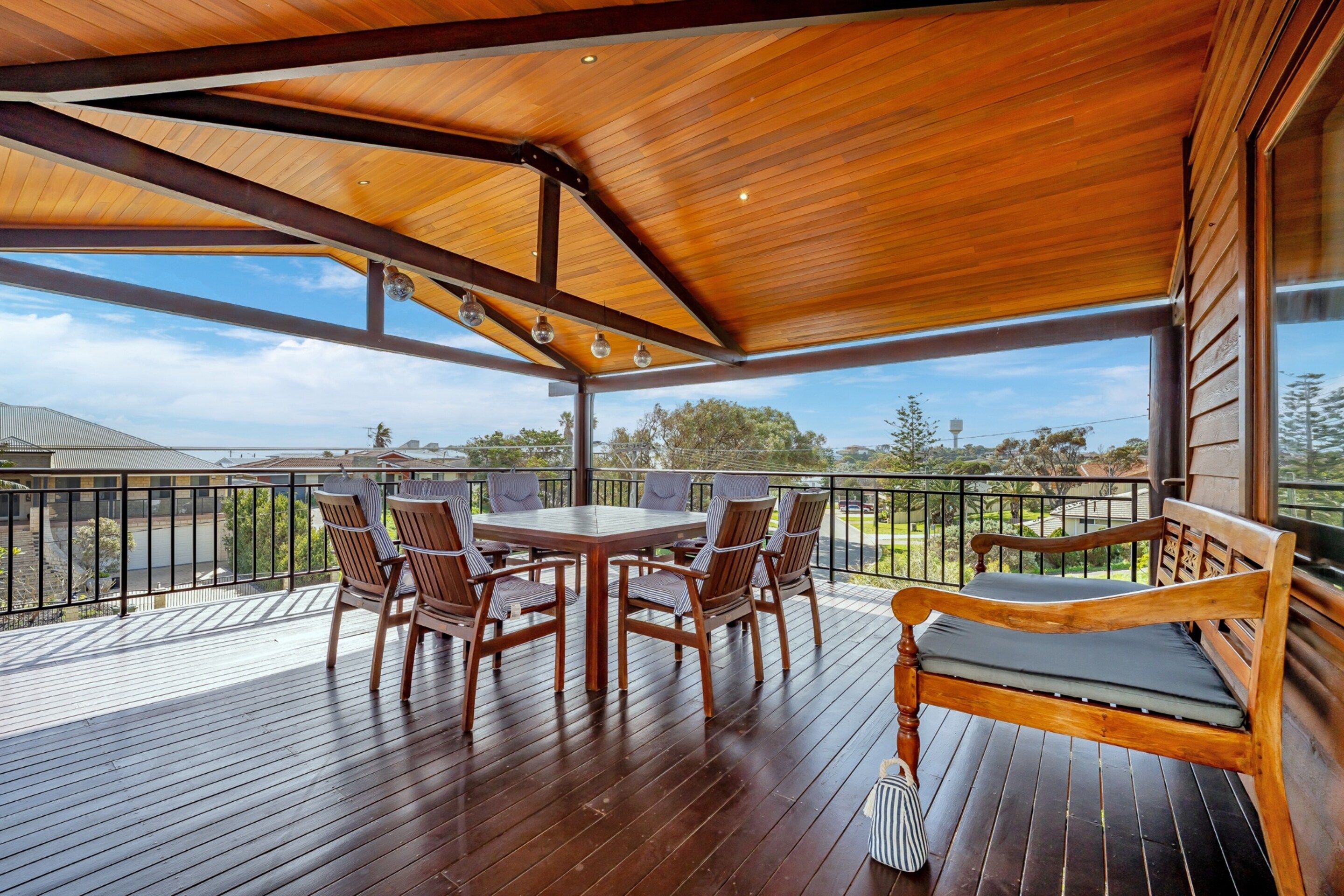 A covered outdoor deck with a wooden table and chairs, a bench, and a view of the surrounding landscape.