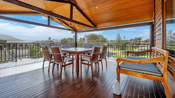 Eine überdachte Terrasse im Freien mit Holztisch und -stühlen, einer Bank und Blick auf die umliegende Landschaft.