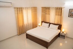 A hotel room with a bed, curtains, a nightstand, and a wall-mounted air conditioner. - Captain's Deck (chanduali)