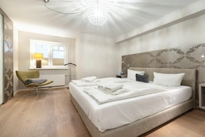 Ein Schlafzimmer mit einem großen Bett, einem Nachttisch, einem Sessel, einem Fenster und einer dekorativen Deckenleuchte.