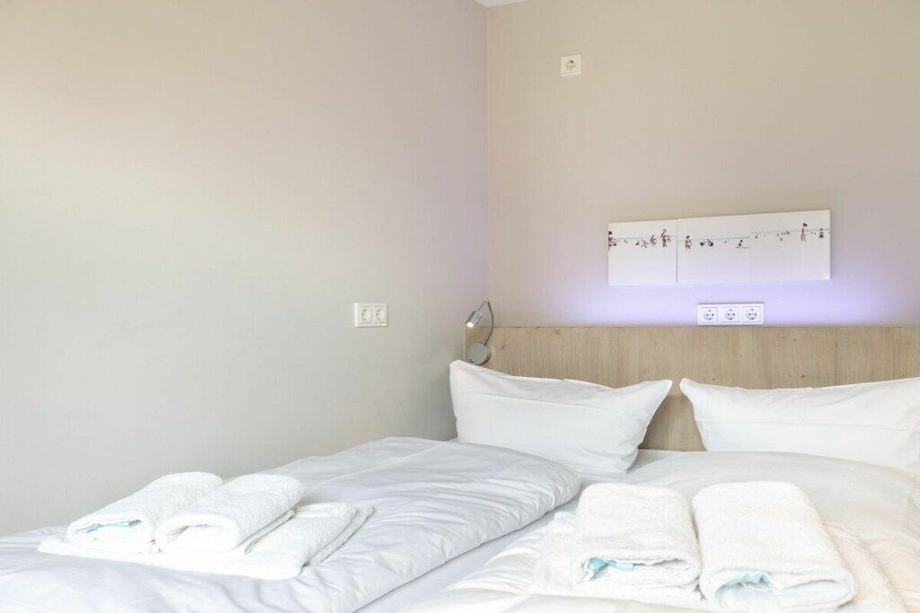 A hotel room with a bed, two pillows, a headboard, and a wall-mounted light fixture.