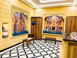 A room with a checkered floor, a wooden cabinet, a small table with a magazine, and a window with curtains.