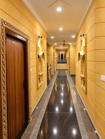 Un pasillo de hotel con puerta de madera, apliques en la pared y una zona alfombrada azul.