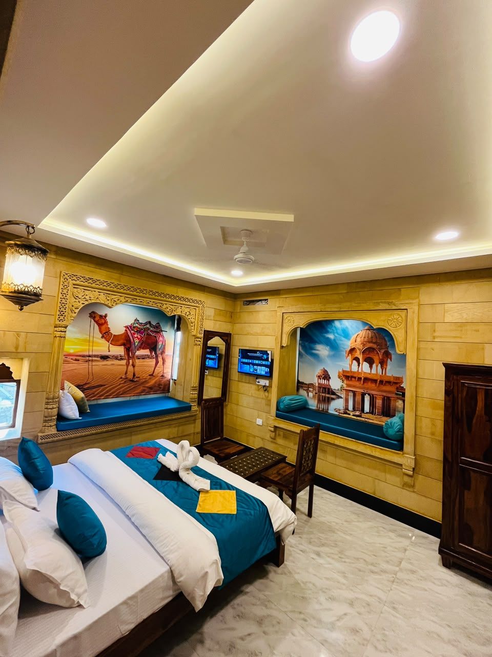 Une chambre d’hôtel comprenant un lit, deux coins salon, une télévision et des fresques murales décoratives.