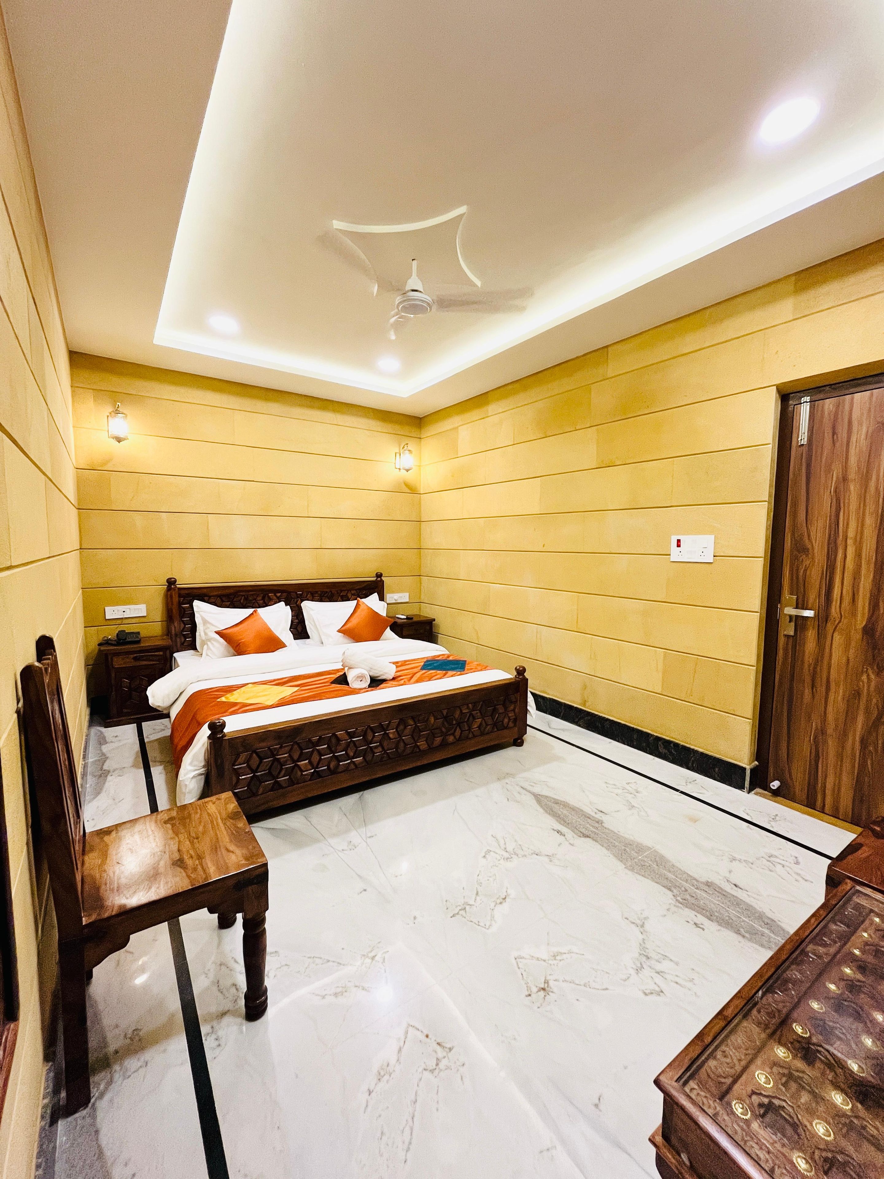 Una habitación de hotel con cama, mesitas de noche, una silla de madera, armario y ventilador de techo.