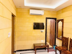 A room with yellow walls, a mounted flat-screen TV, a wooden door, and a small table.