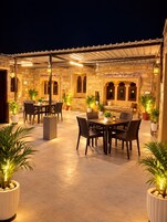 An outdoor patio area with stone walls, a seating area with tables and chairs, and potted plants.